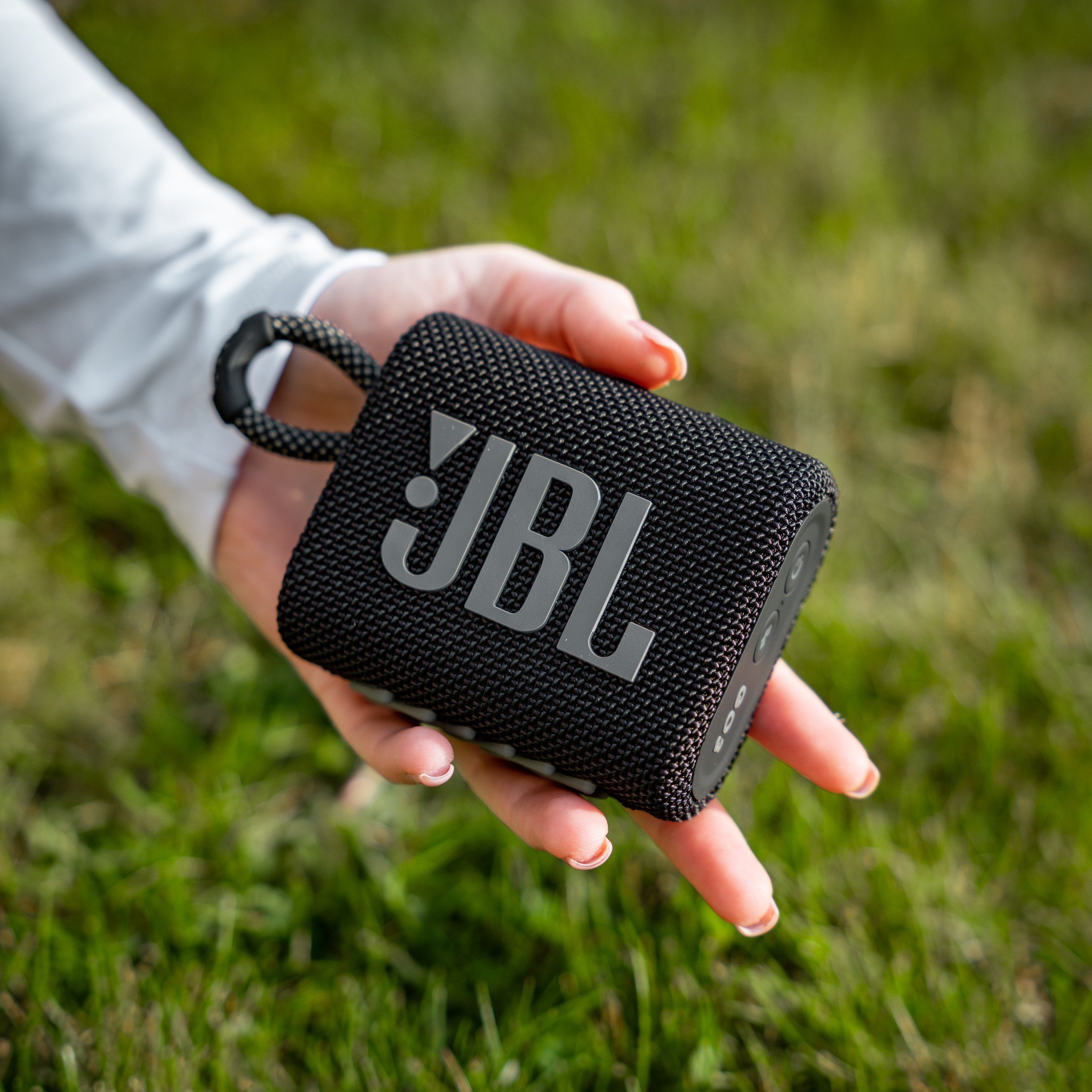 Hand holding a black JBL speaker over the grass
