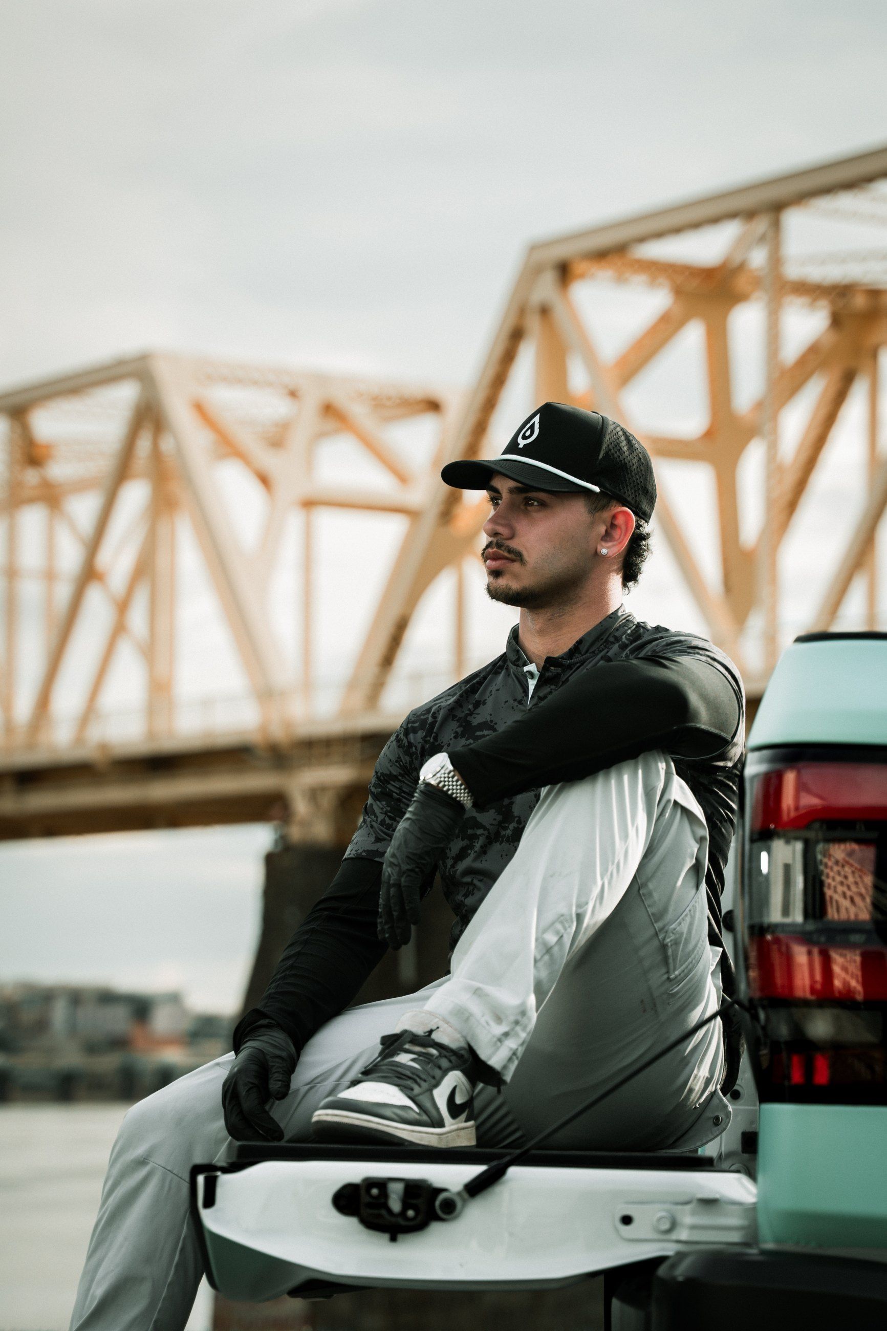 Technician resting on a tailgate in front of an orange truss bridge