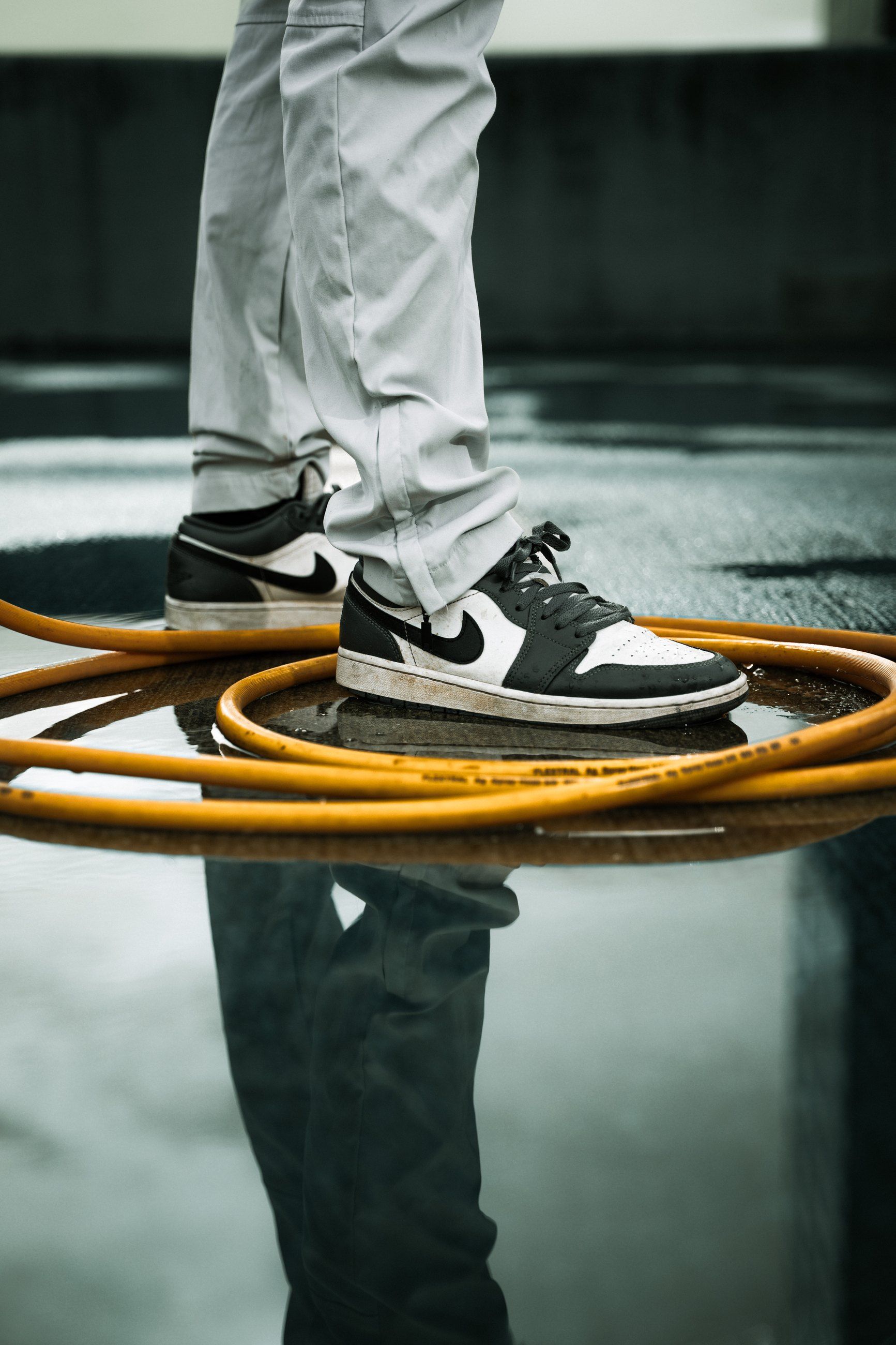 Sneakers standing in coils of orange hose, reflected in a puddle