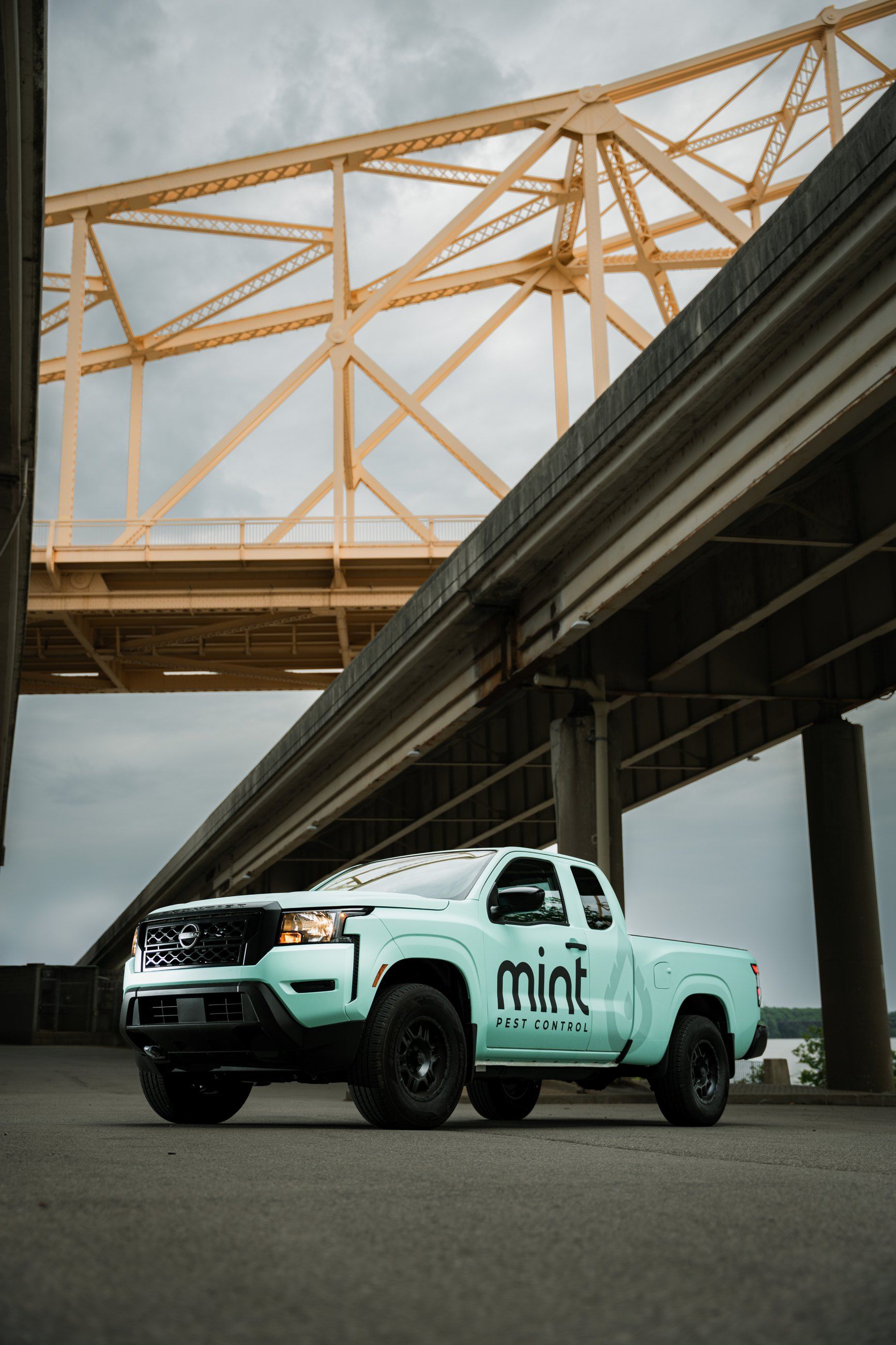 Mint-green pickup parked under a highway and a steel bridge