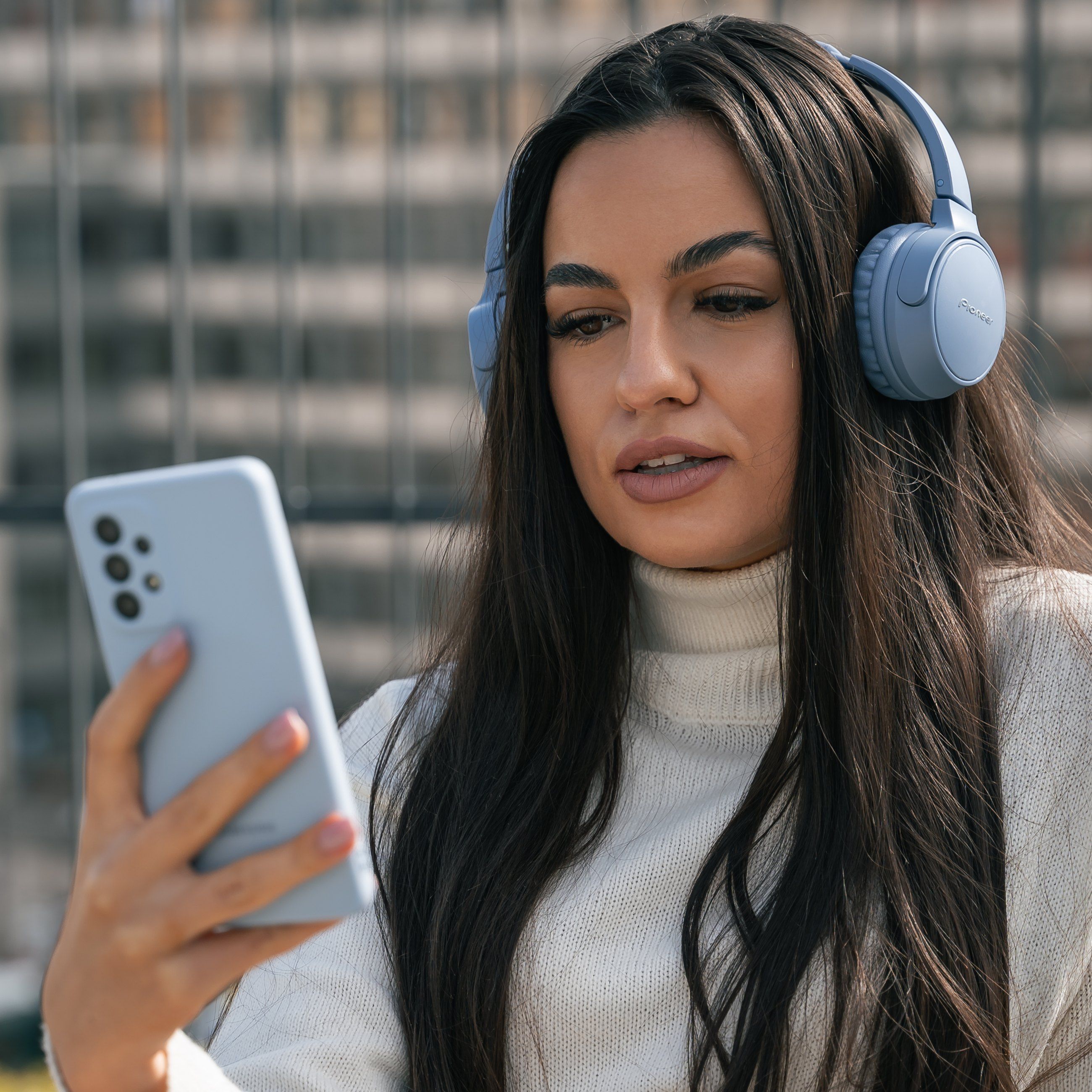 Woman in headphones scrolling on a pale blue phone