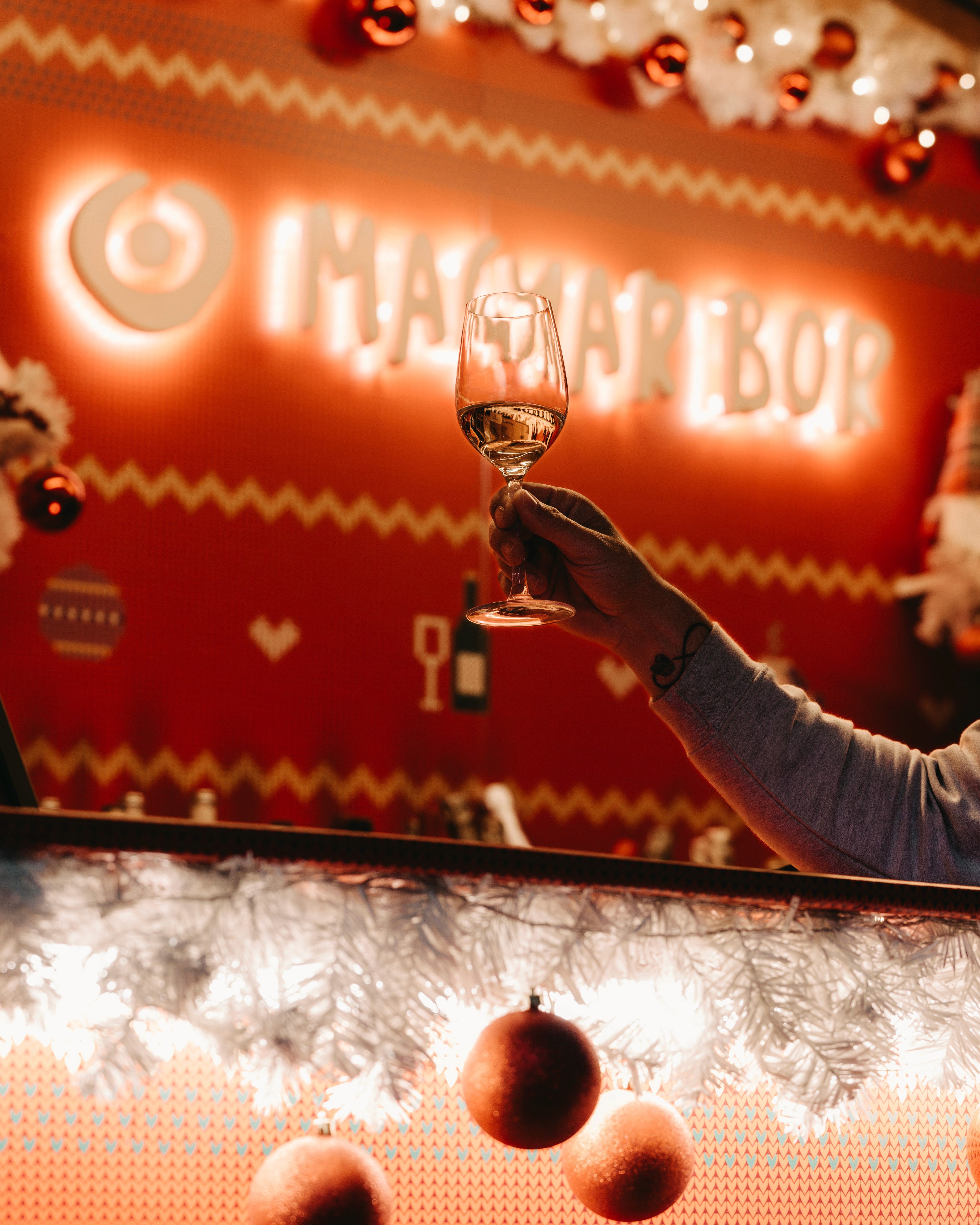 A glass of wine raised in front of a glowing Magyar Bor neon sign